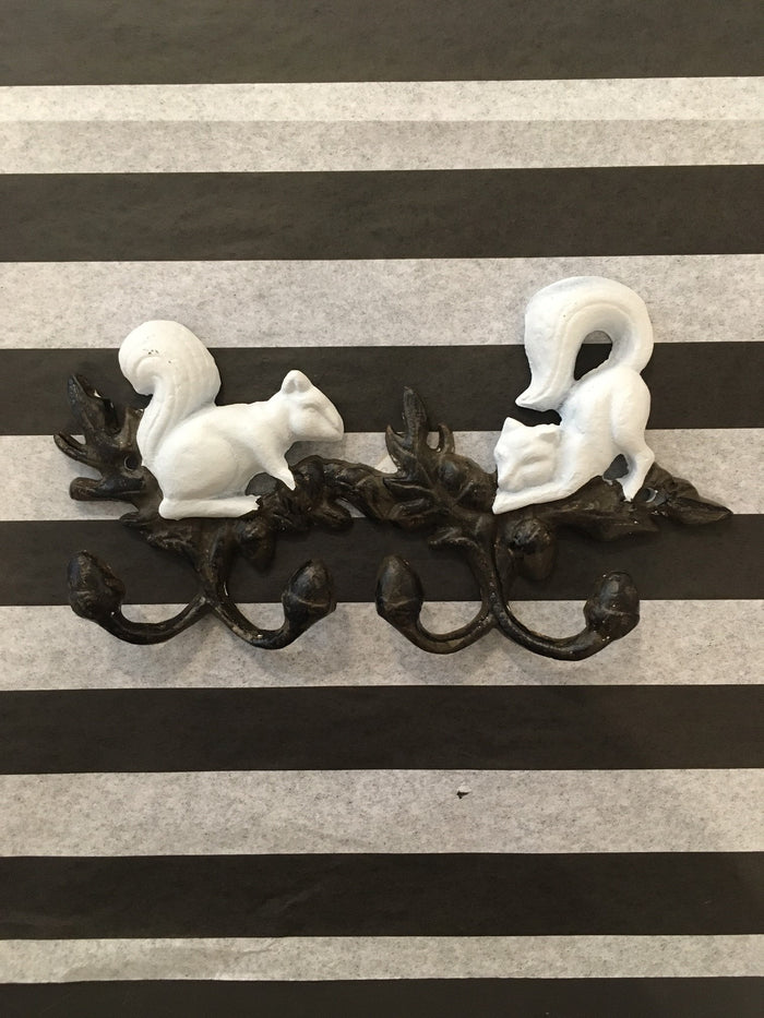 A cast iron wall hanger featuring two white squirrels and four dark brown acorn hooks.