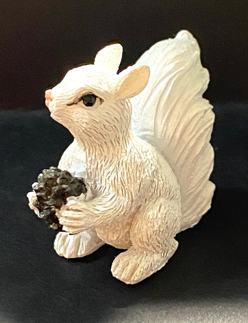 A miniature white squirrel resin figurine holding a pinecone.