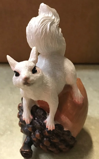 A white squirrel resin figurine perched on top of an acorn.