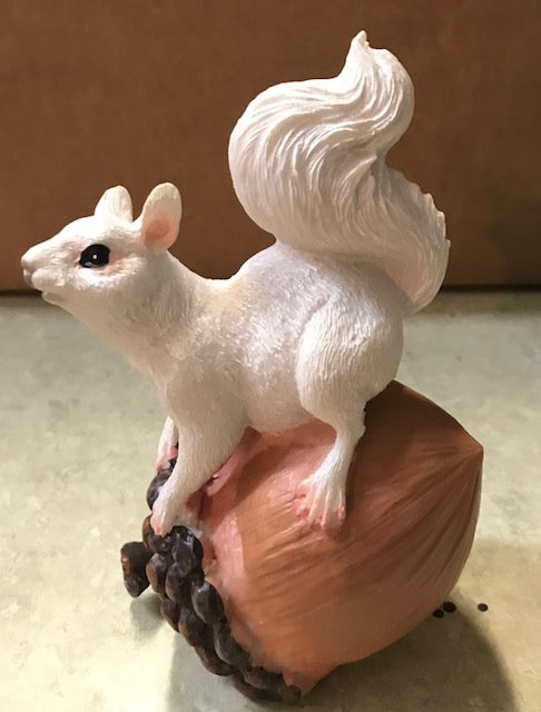 Side view of a resin white squirrel perched atop an acorn