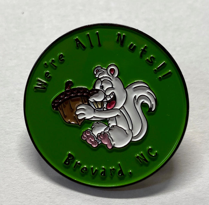 We're all nuts!! Brevard, NC lapel pin. This lapel pin has a nutty white squirrel holding an acorn on a green background.