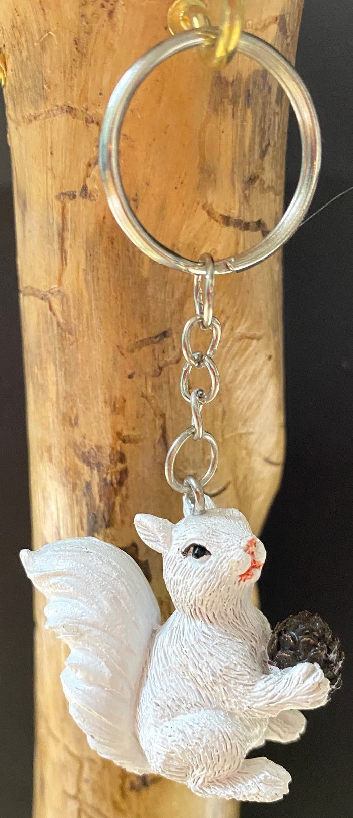 A miniature white squirrel holding a pine cone resin key chain.