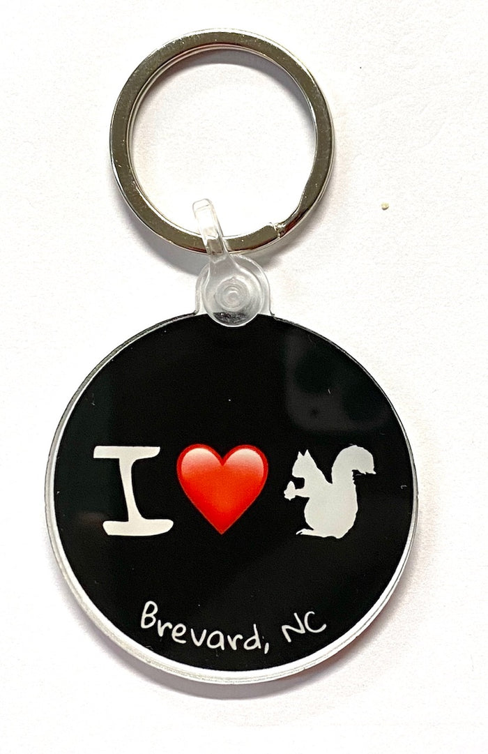 A black acrylic circle key chain with the text 'I Love White Squirrels', an an illustration of a white squirrel, and 'Brevard, NC' on a keyring.