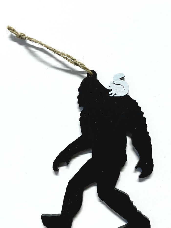 A laser cut wood ornament in the shape of a Sasquatch with a white squirrel on his shoulder. Includes a string attached for hanging.